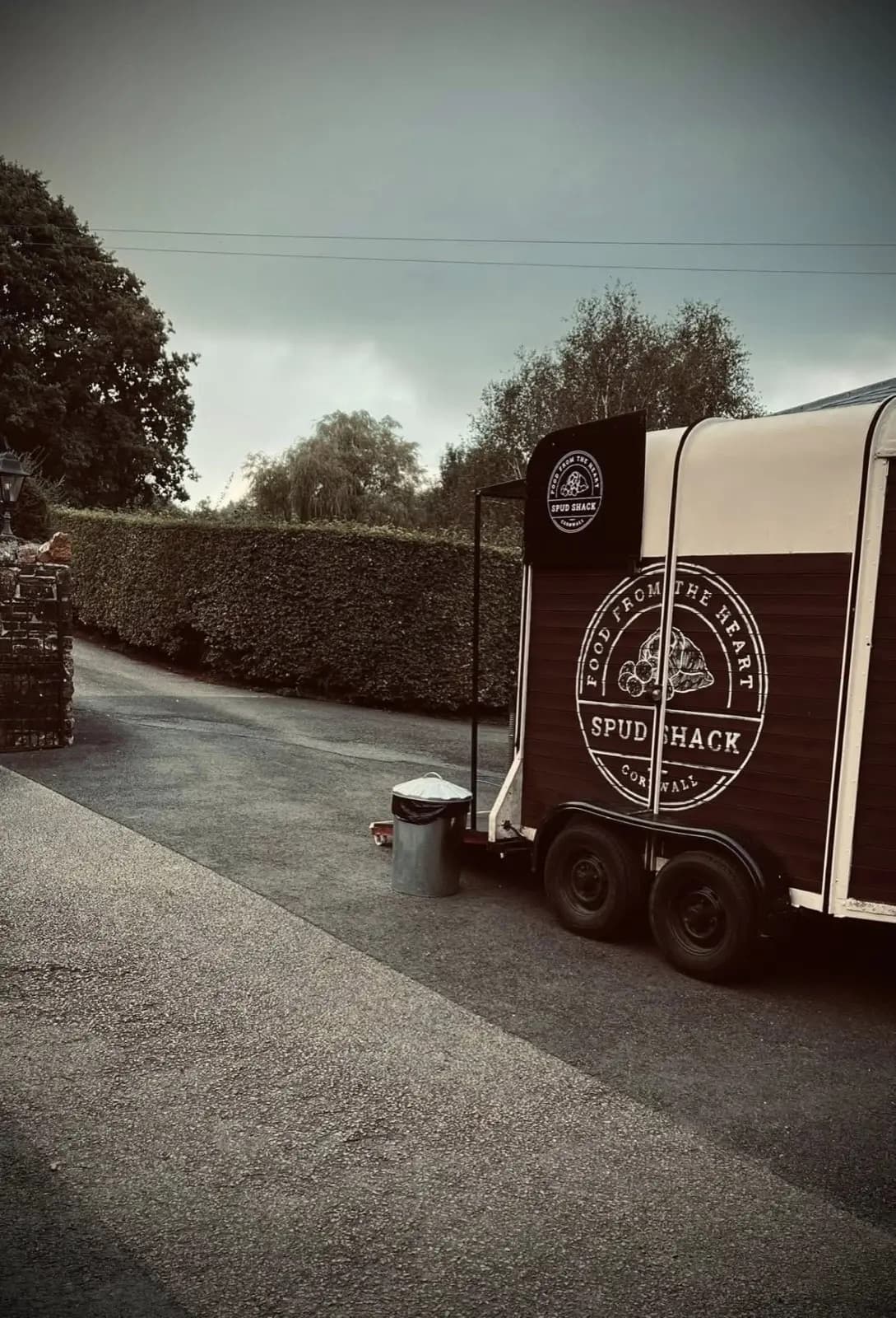 The Spud Shack horsebox parked on the driveway — full side view of the painted Food From The Heart · Spud Shack logo, hedge and lamp post in the background